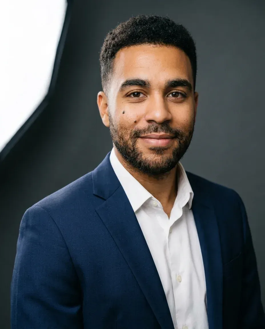 Corporate headshot of the same man in a navy suit jacket and white shirt on a charcoal backdrop